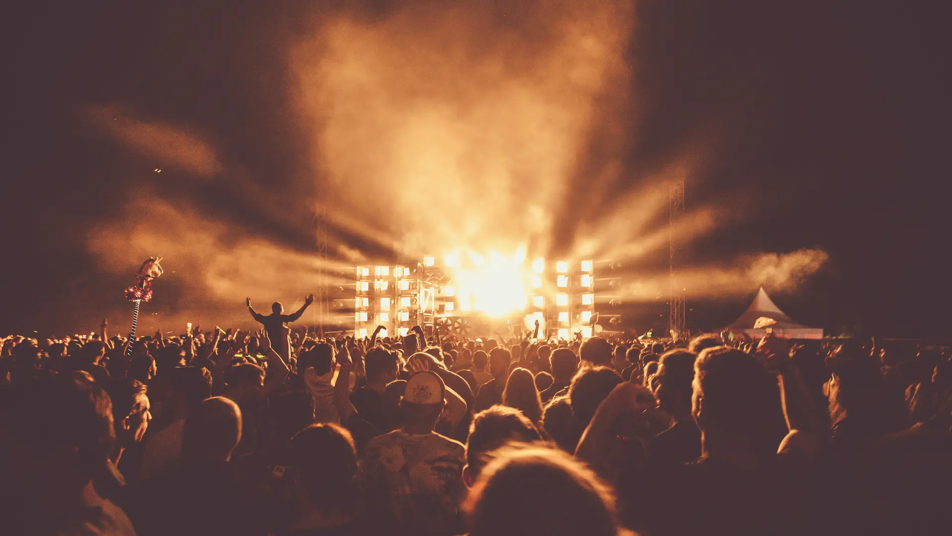 A crowd in silhouette before a stage blazing with orange light and haze.