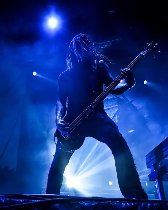 A long-haired guitarist on stage, back-lit in blue.