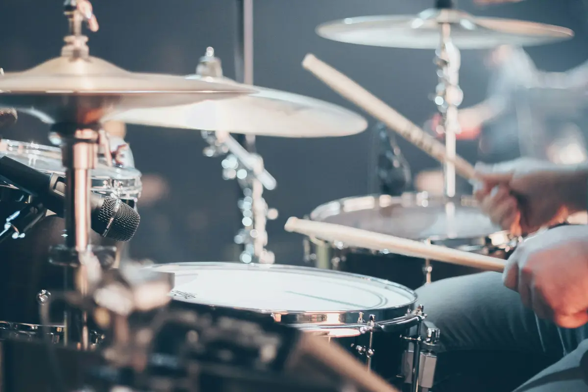 A drummer mid-stroke behind cymbals and a snare, under cool stage light.
