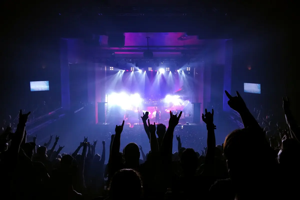 Raised hands silhouetted against a stage glowing purple and white.