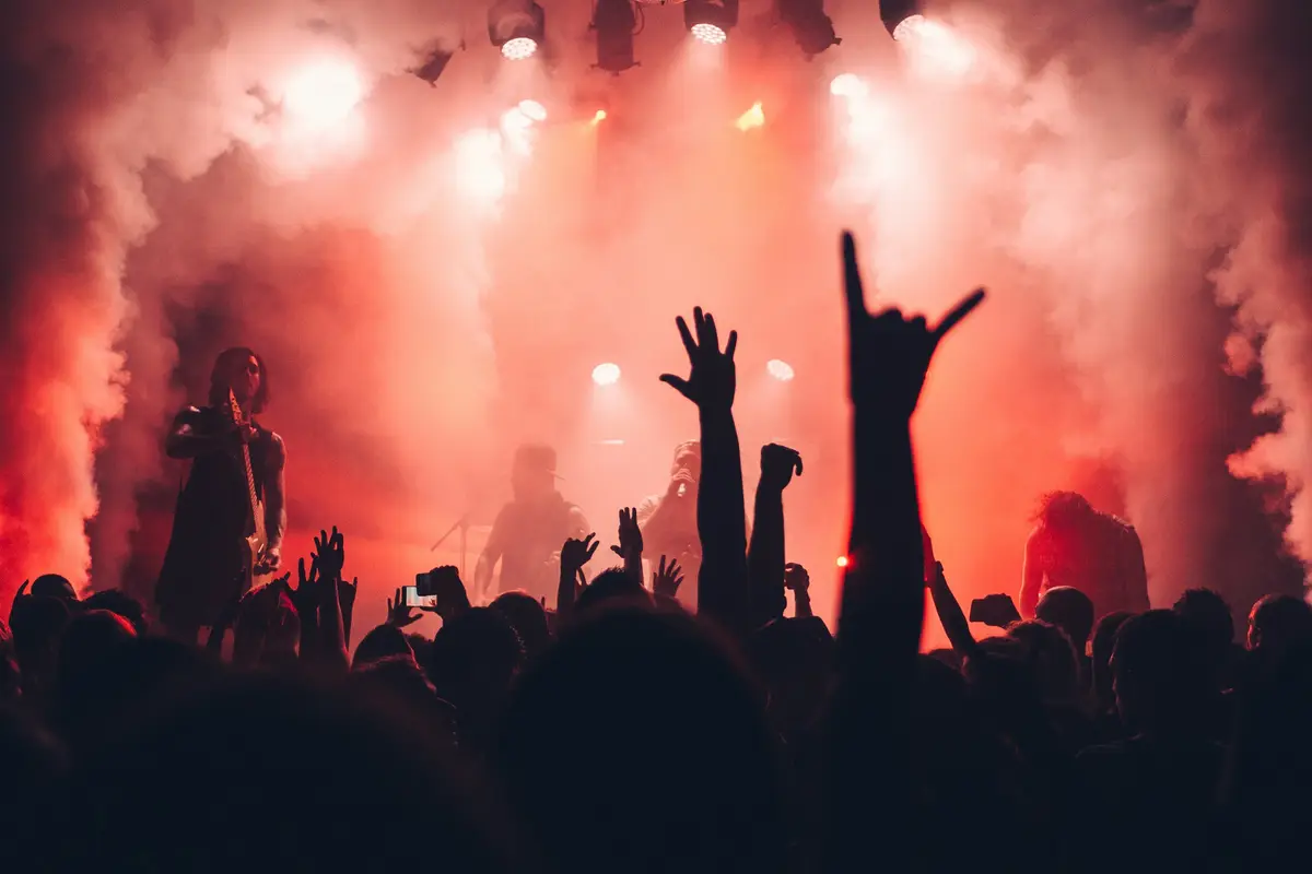 Hands making the horns sign in red smoke in front of the stage lights.